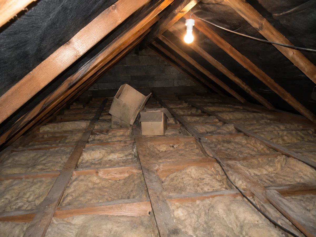Loft before work: bare joists, thin old insulation and a single hanging bulb