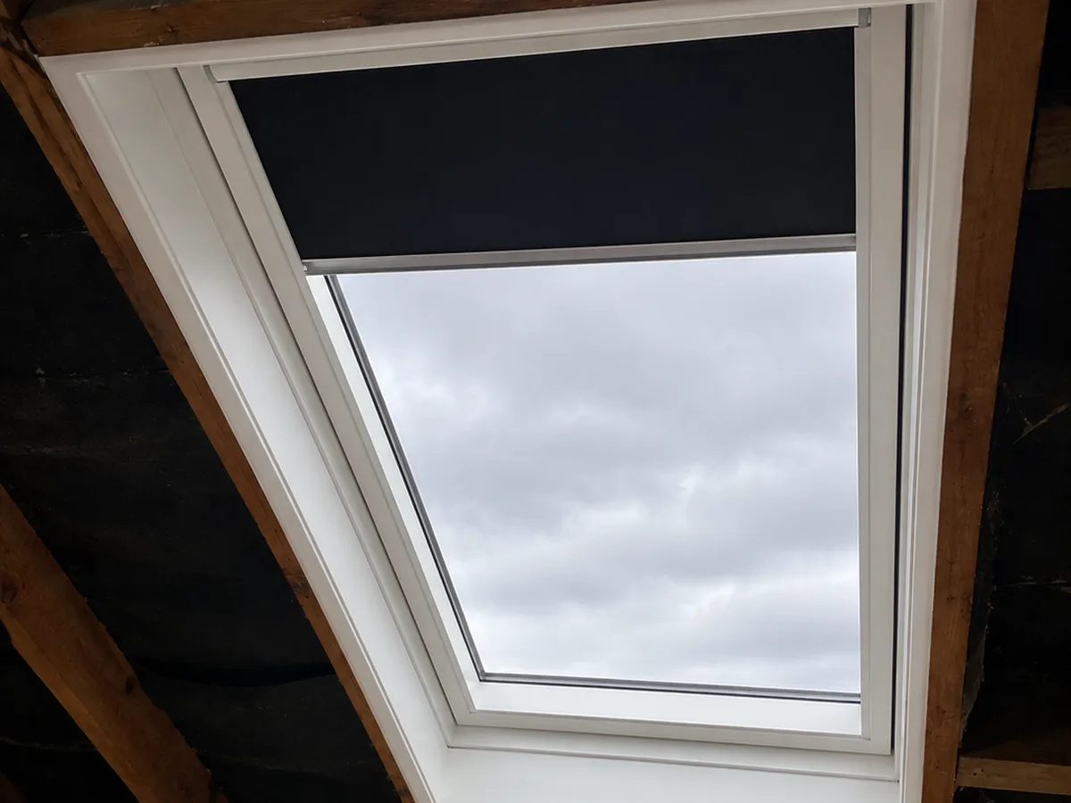 The same opening after replacement: new centre-pivot roof window with a blackout blind part-lowered