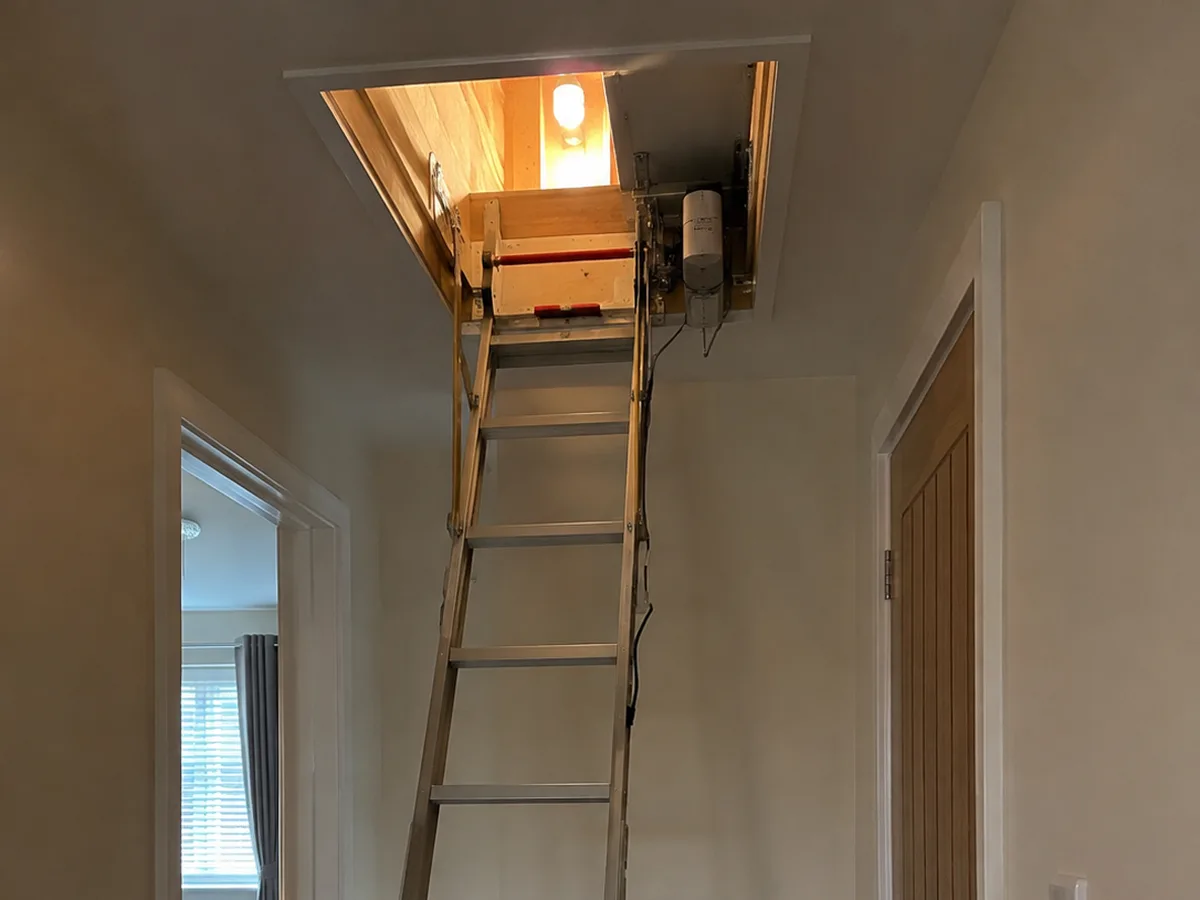Electric loft ladder extended down from an open hatch into a modern hallway