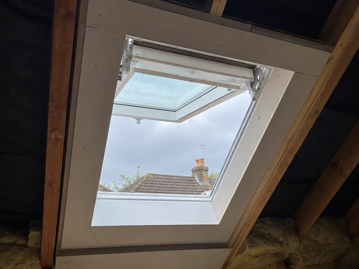 Top-hung escape roof window propped open from inside the loft, neighbouring rooftops beyond