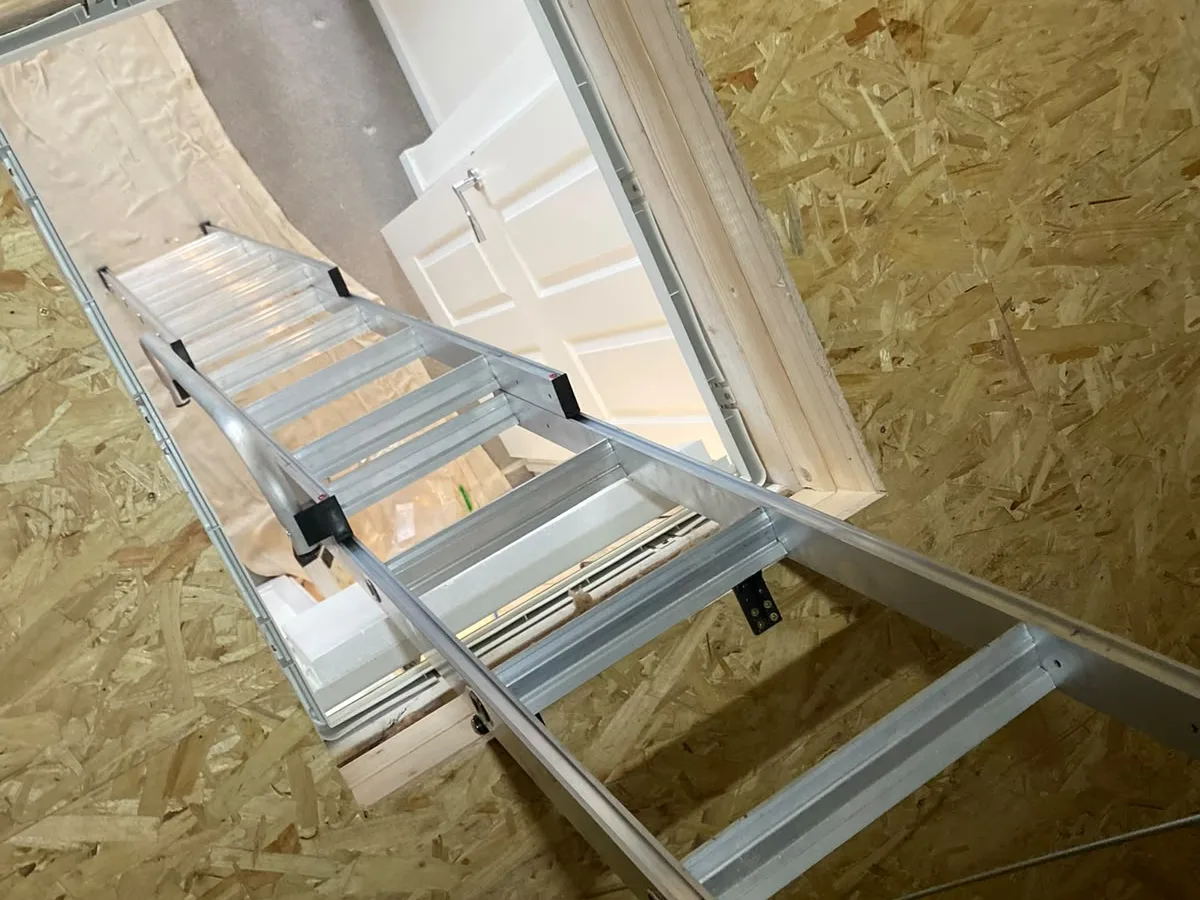 Looking down an aluminium loft ladder through the open hatch to the landing