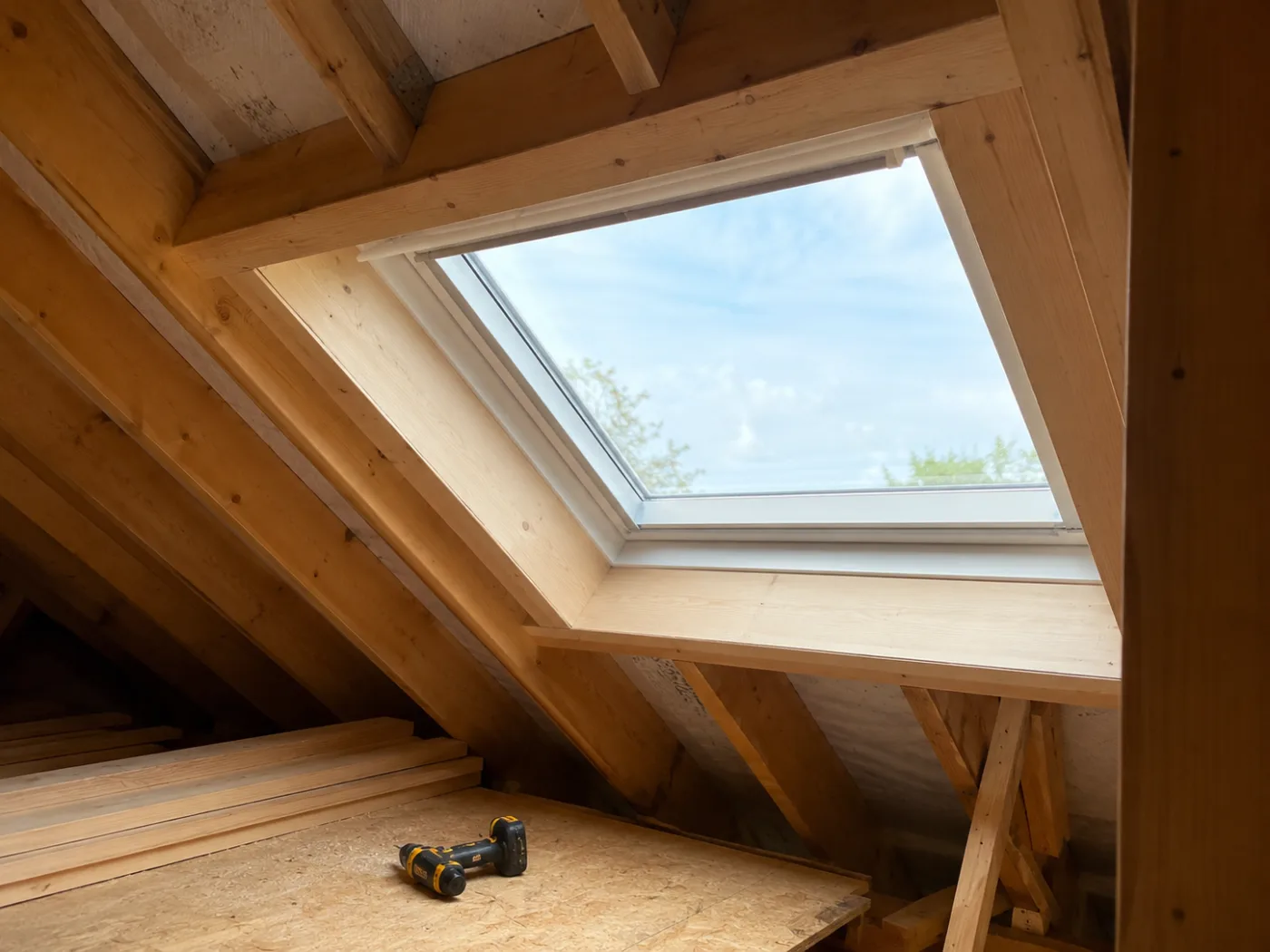 Roof window set into the rafters with a timber-lined reveal, sky visible through the glass
