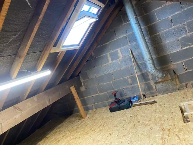 Boarded loft under an existing roof window, blockwork gable and soil pipe beside