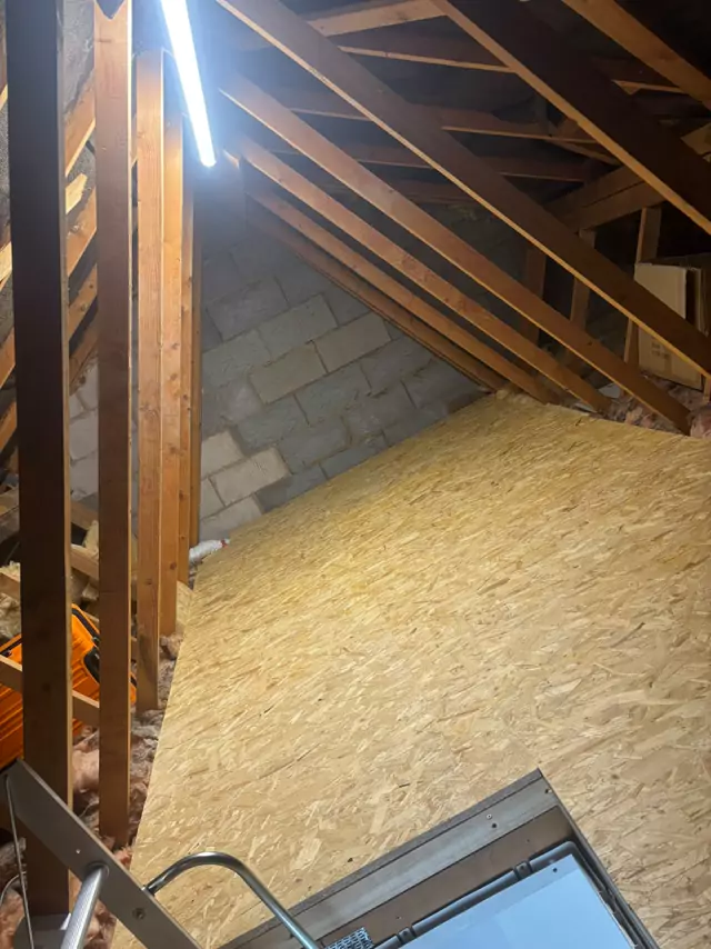 Boarded loft between trusses up to a blockwork gable, ladder at the hatch