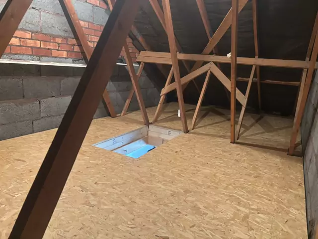Boarded floor round a hatch in an older loft with blockwork walls