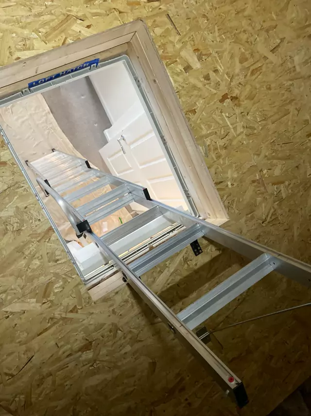 Folding aluminium loft ladder through a timber-lined hatch, seen from the loft